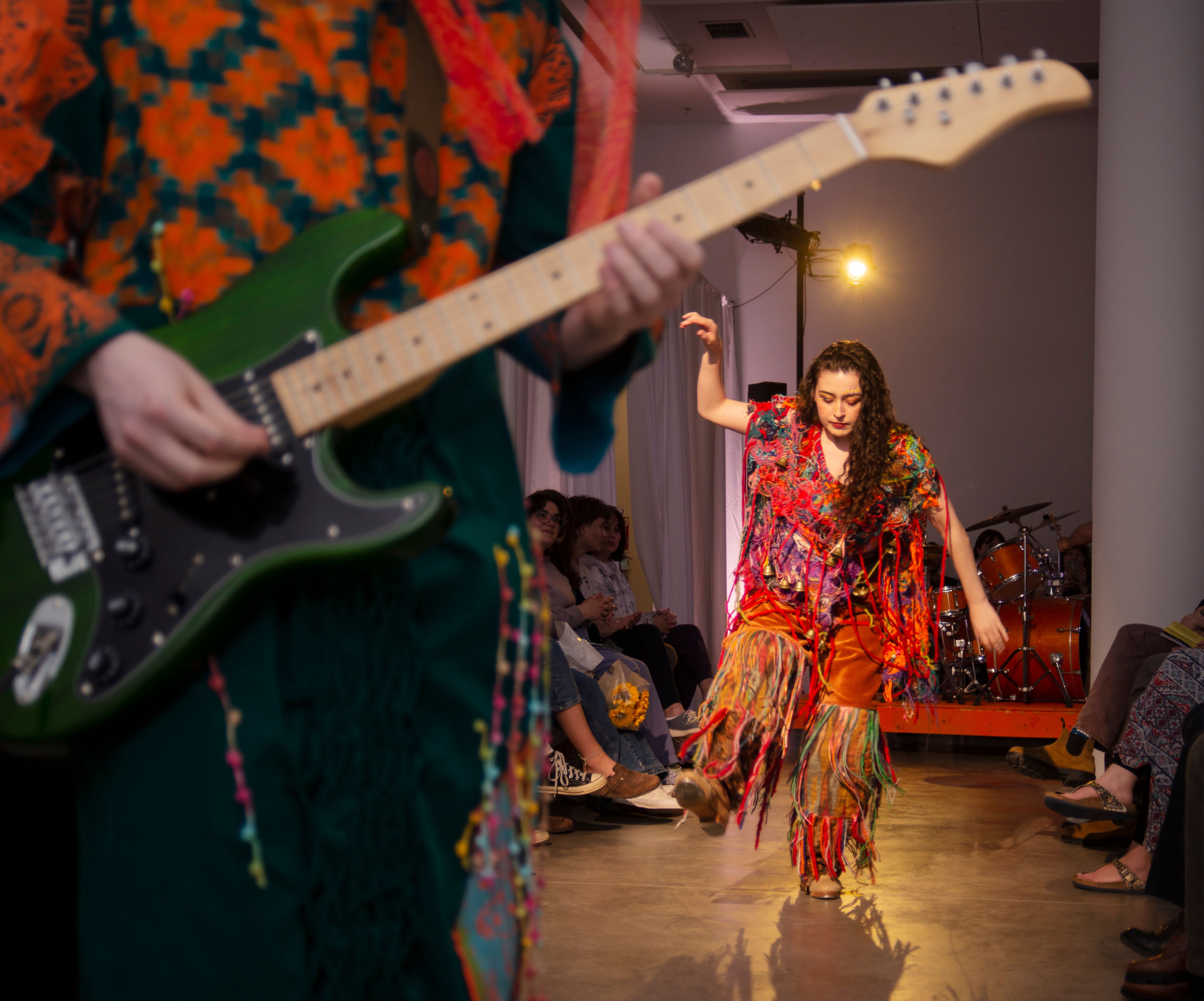 Two models wearing hippie-inspired garments, one is dancing while the other plays guitar.