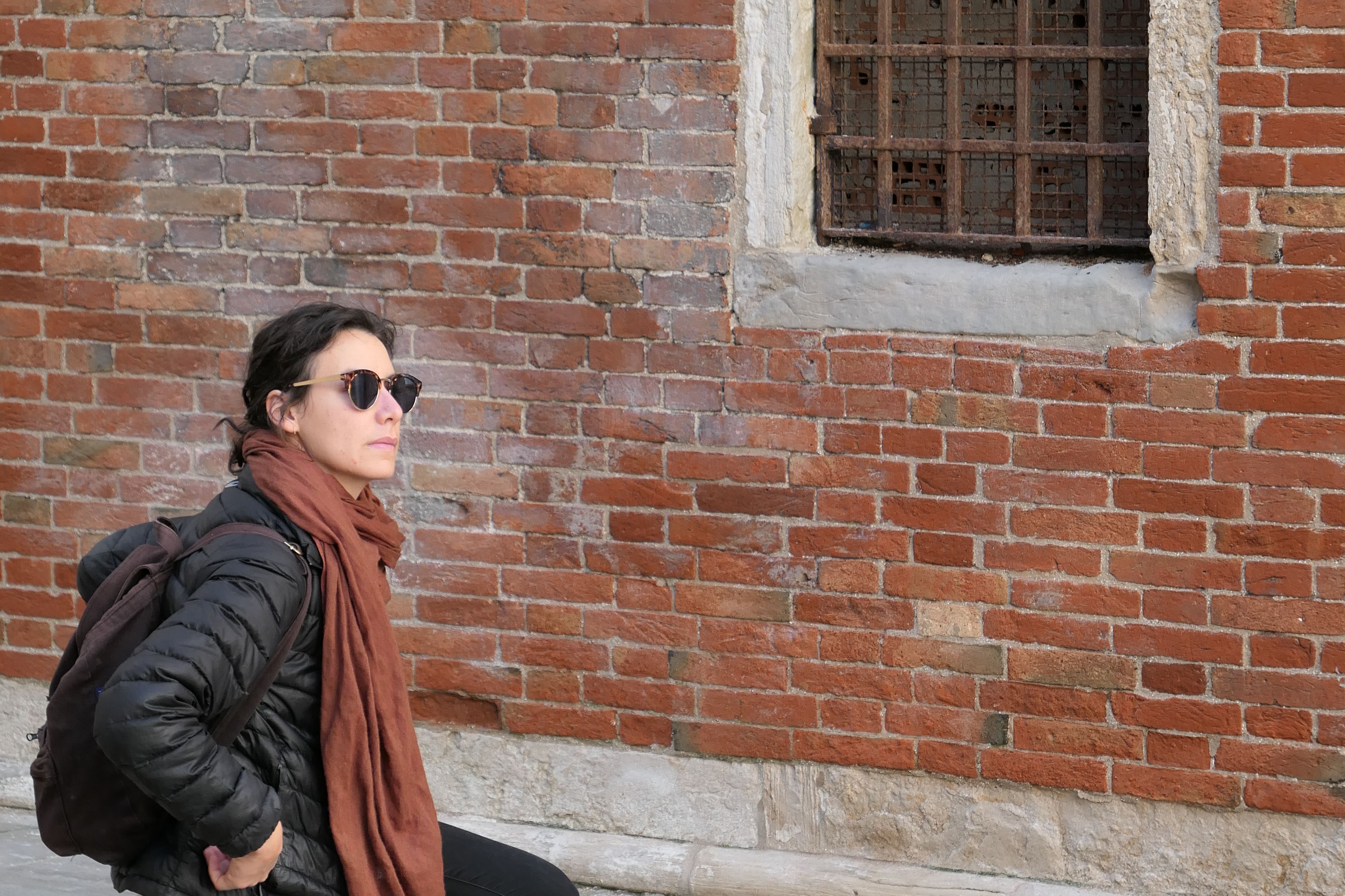 An MFA student sitting facing a brick wall with a grated window.