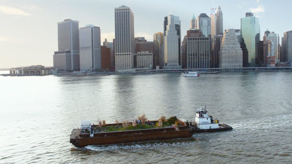 A view of a grassy area atop a large boat in front of a city skyline.