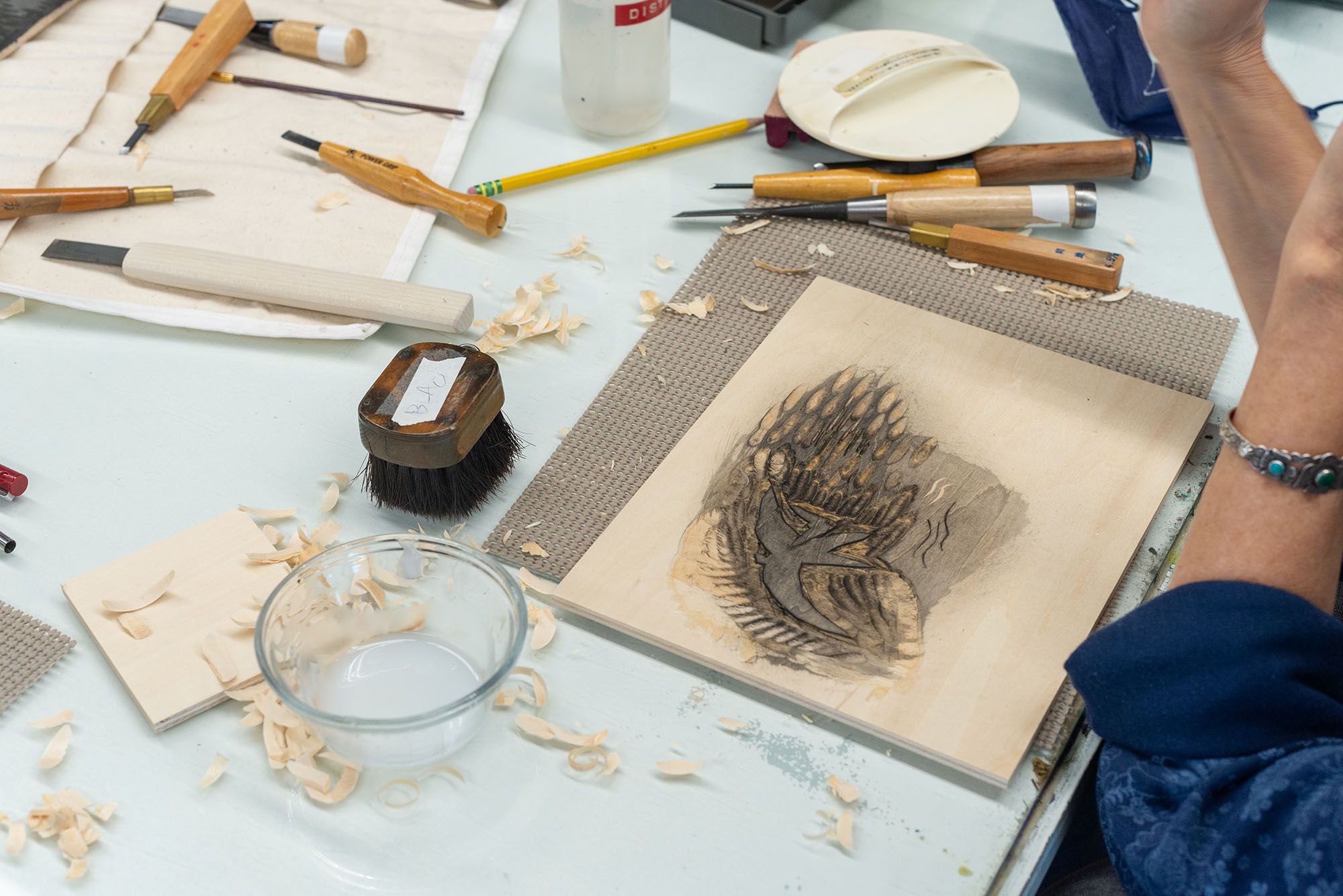 In-process woodcut surrounded by wood shavings and carving tools.