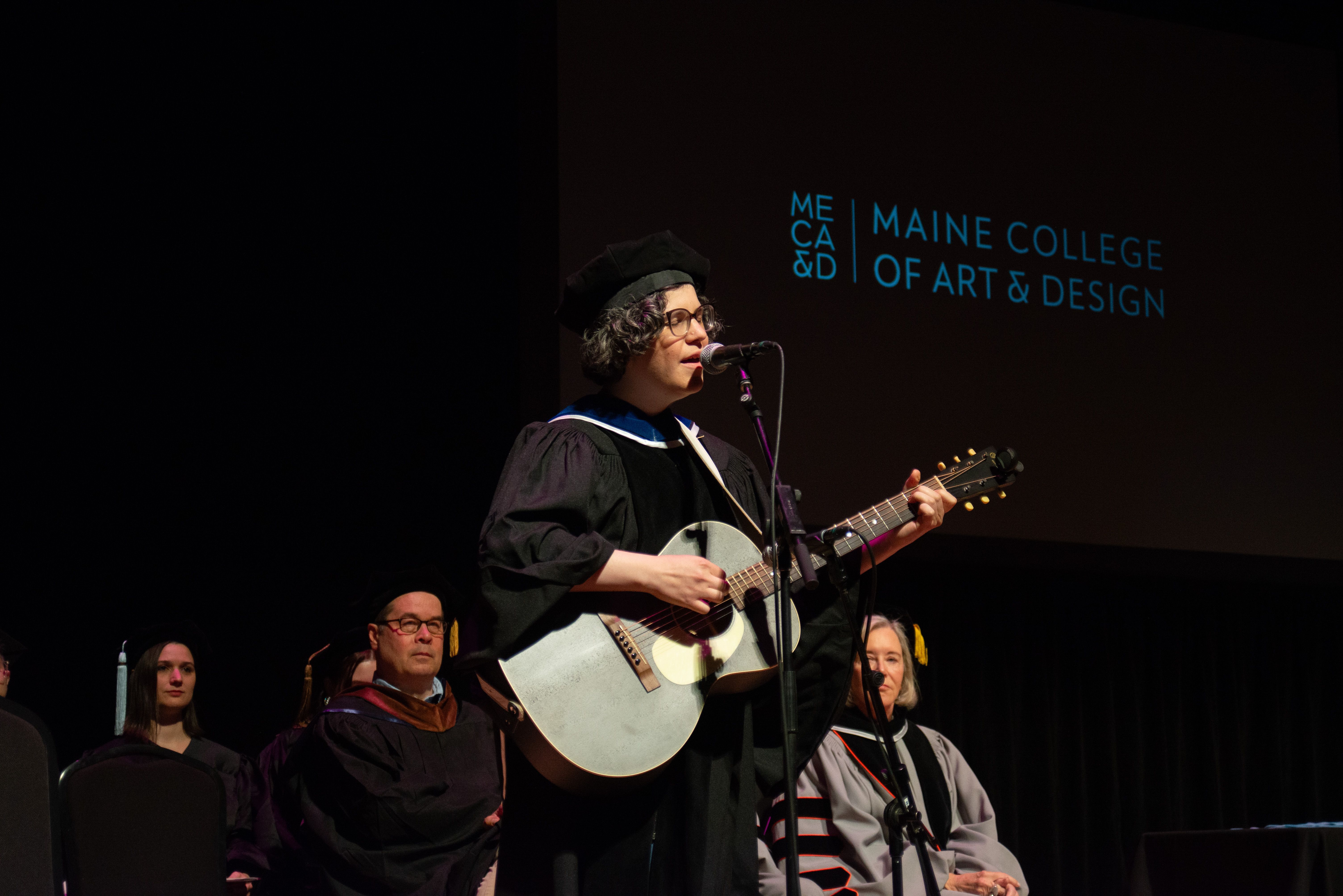 Rebecca Sugar playing guitar in graduation regalia