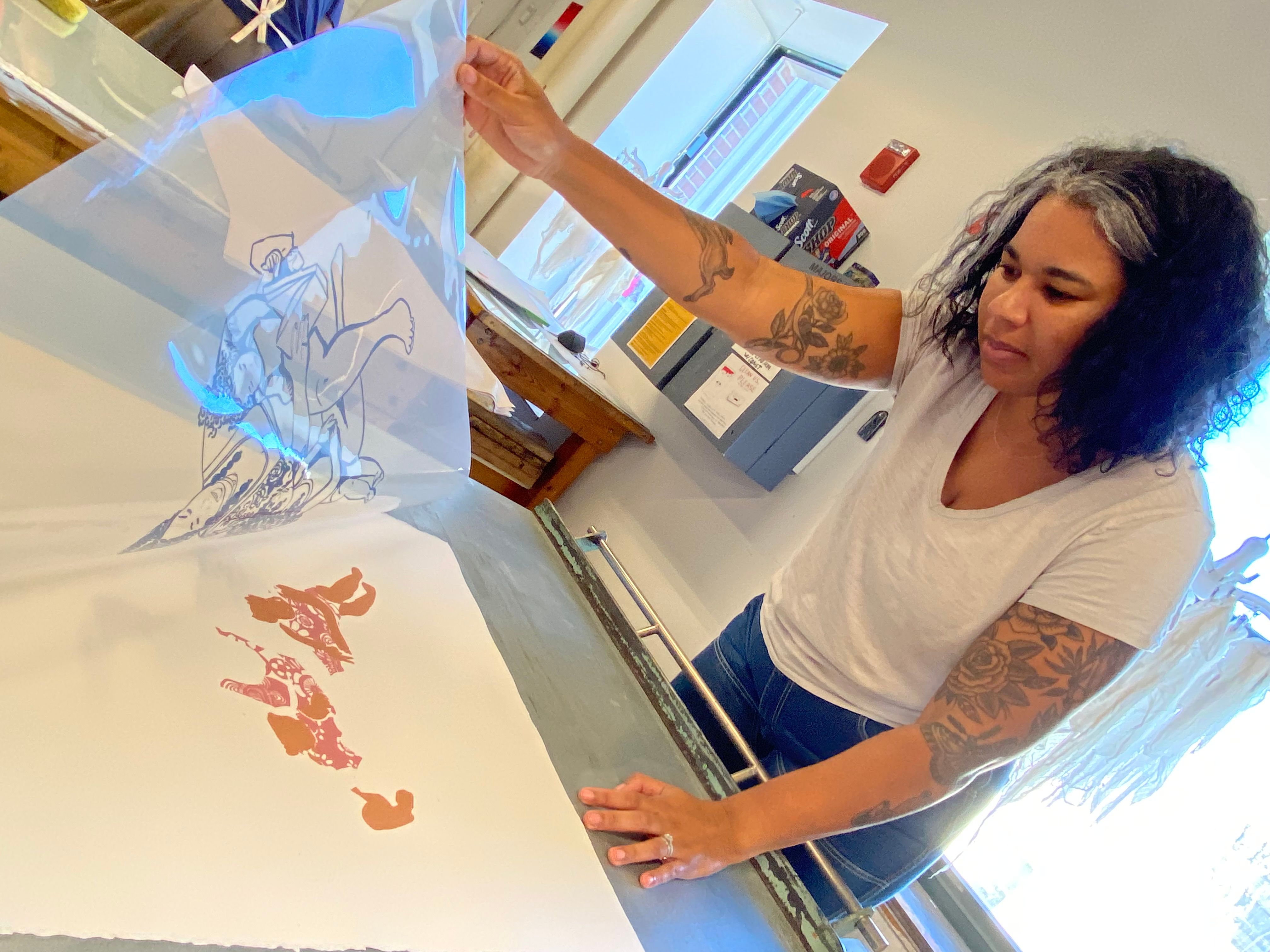 An artist lifts up a layer of acetate off of a print to check registration.