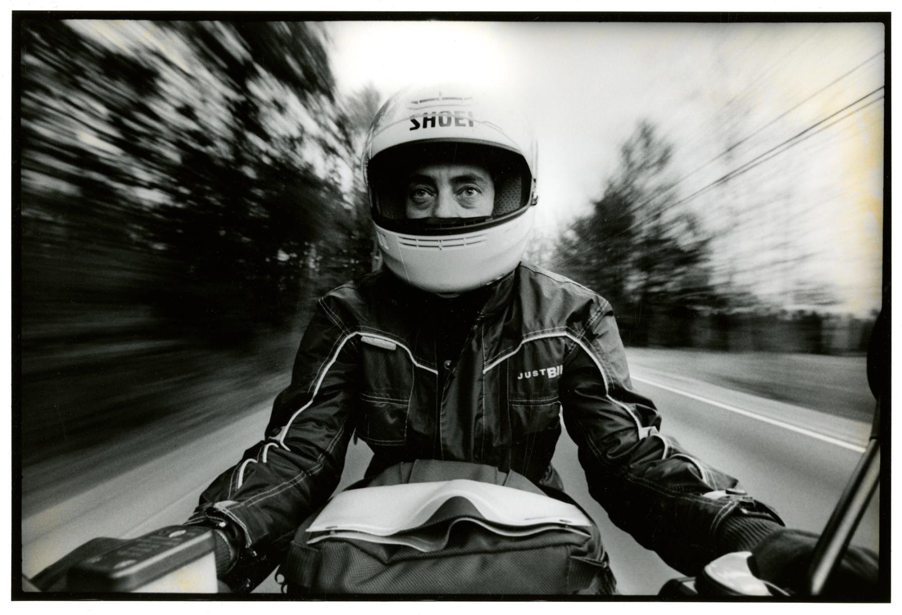 A photograph of a person riding a motorcycle with a blurred background.