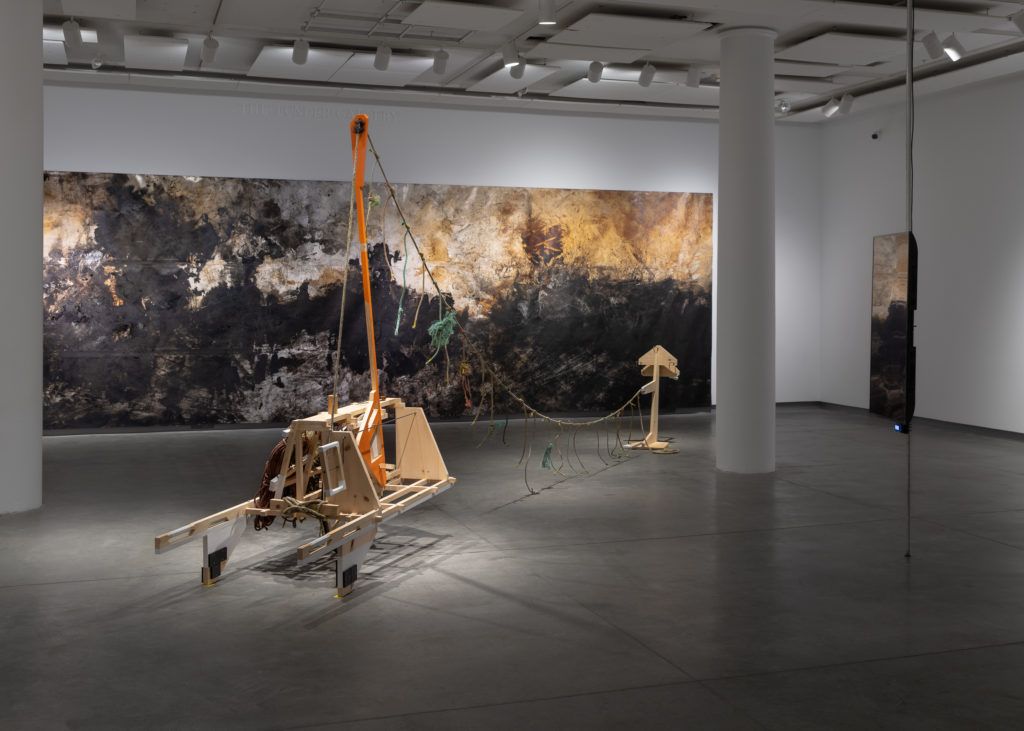 A wooden cart-like sculpture in front of a large abstract painting.