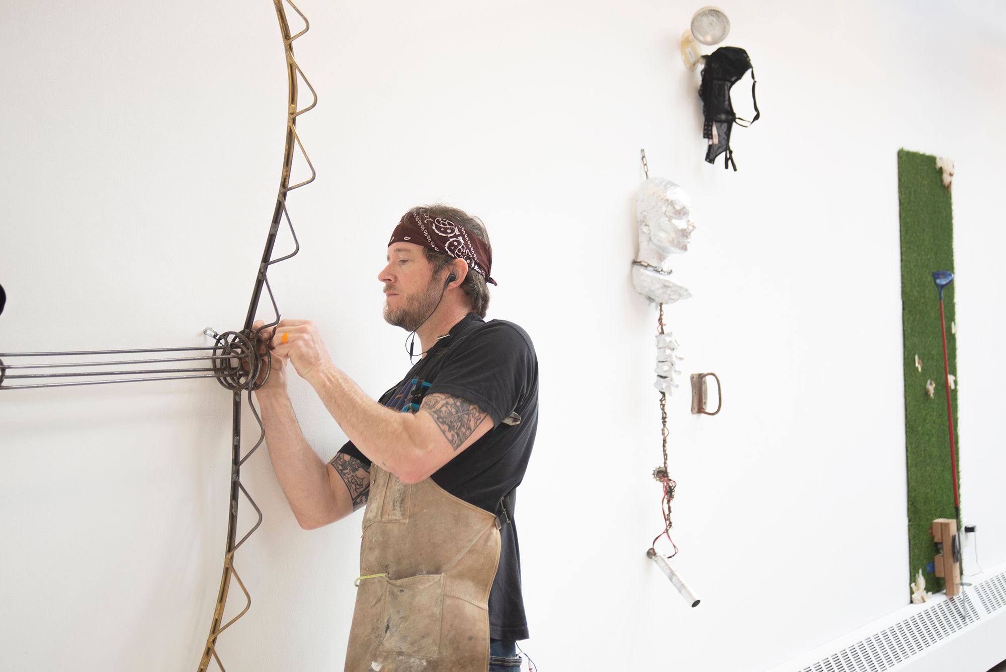 Student installing a bear-trap-inspired sculpture on a wall next to other sculptures.