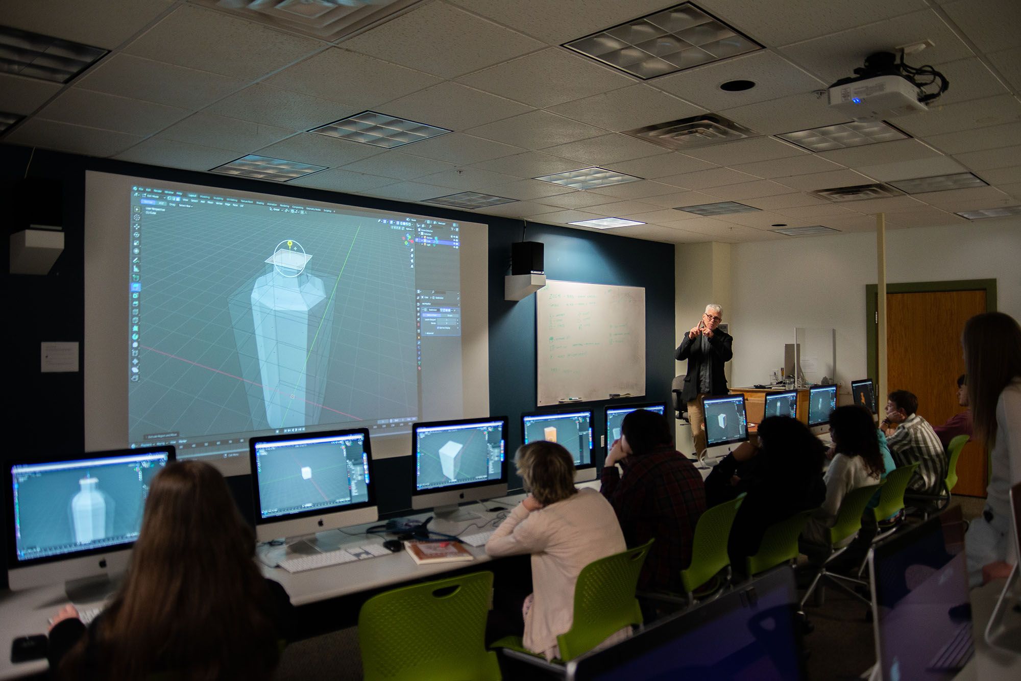 A classroom of students working on computers during a demonstration of 3D modeling.