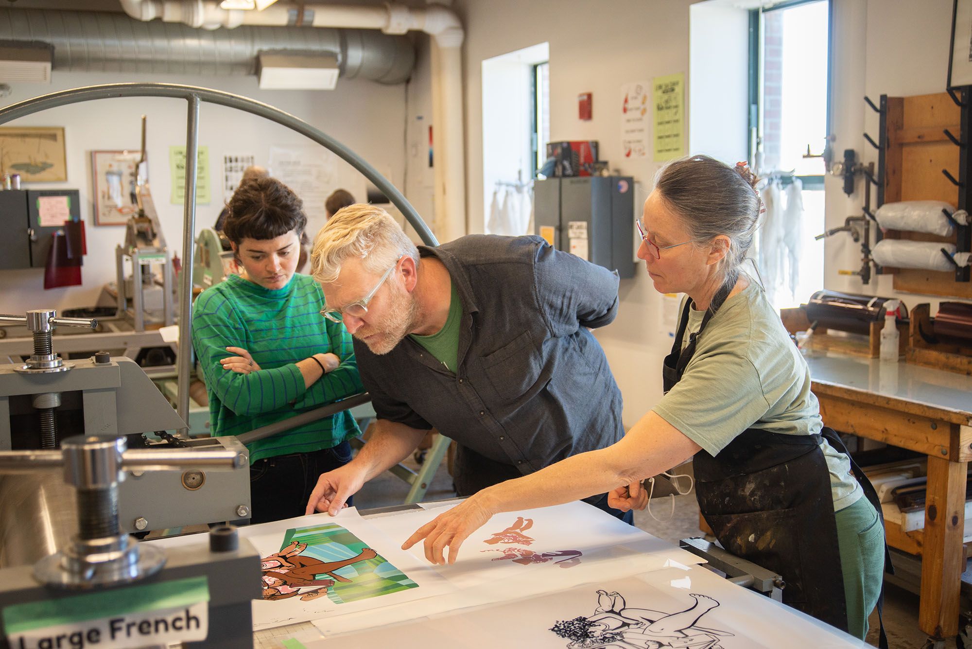 Faculty members looking and pointing at an in-process silkscreen and lithography print.