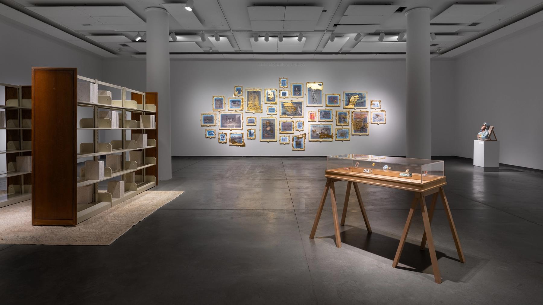 Installation view of work included in the Objects and Power exhibition. A gallery of frames is on the back wall, sculptural book shelves on the left, and two sculptural pieces on the right.