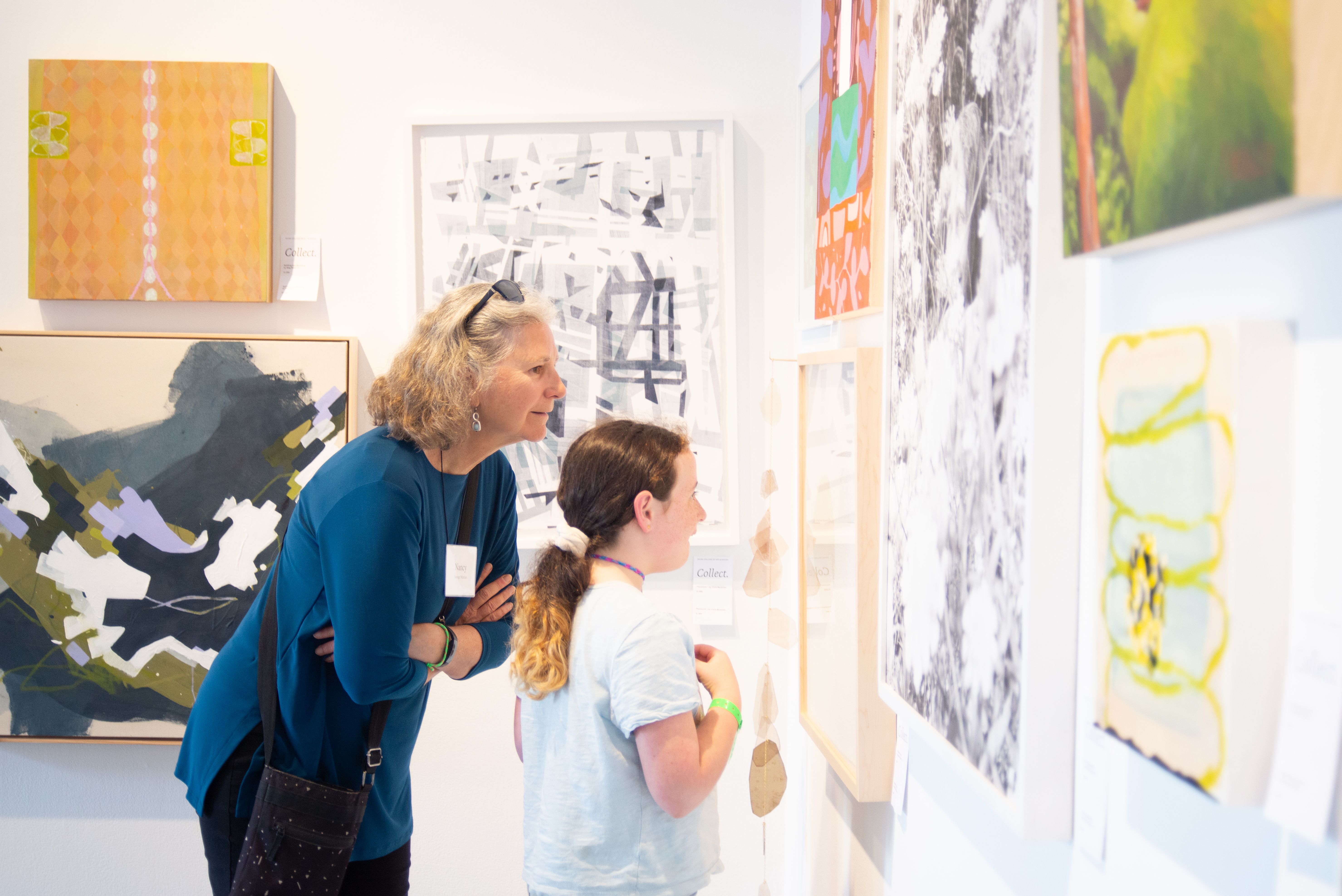 A woman and a child leaning toward an art piece hanging on a wall.