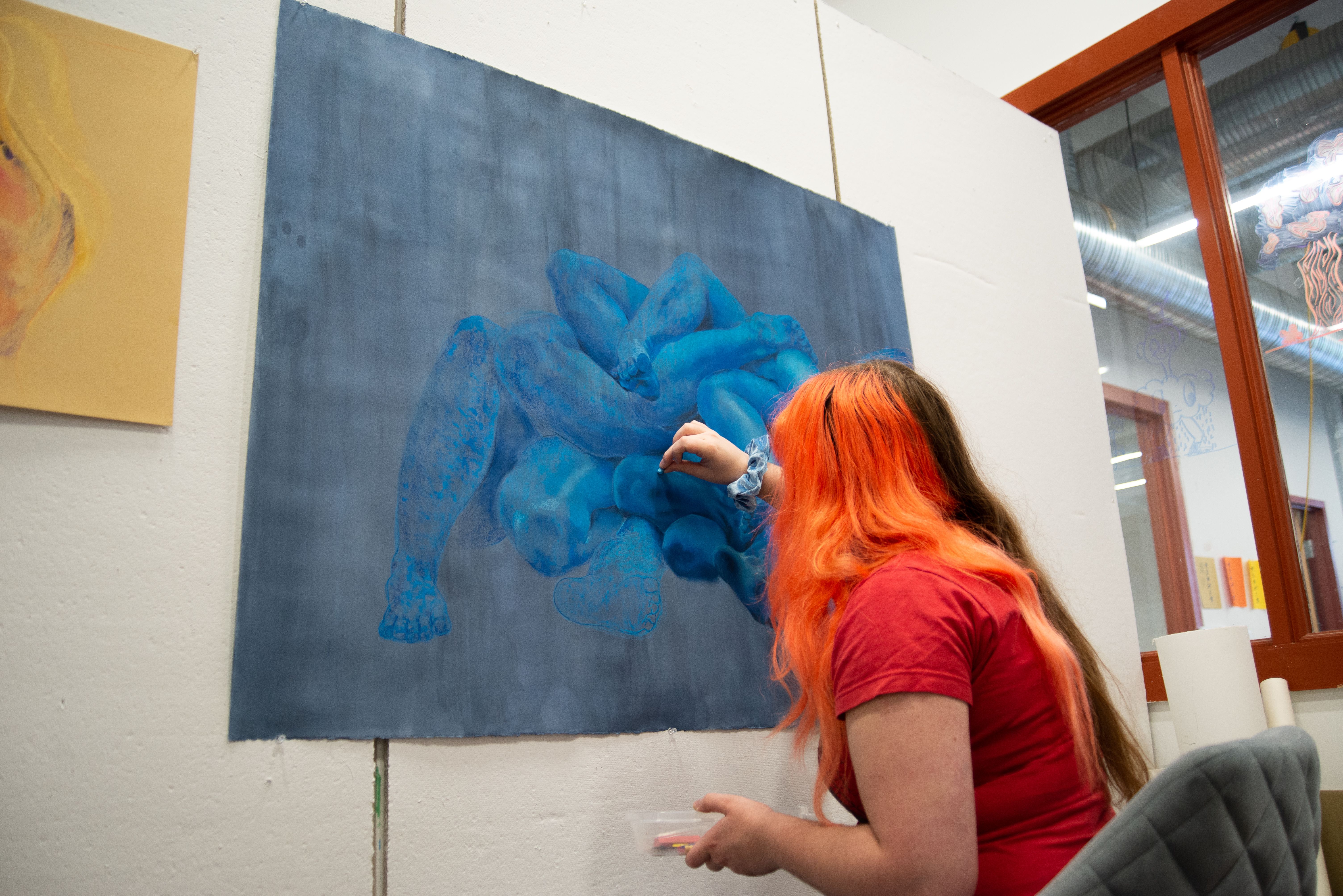 MFA student working on a blue painting of disembodied limbs.