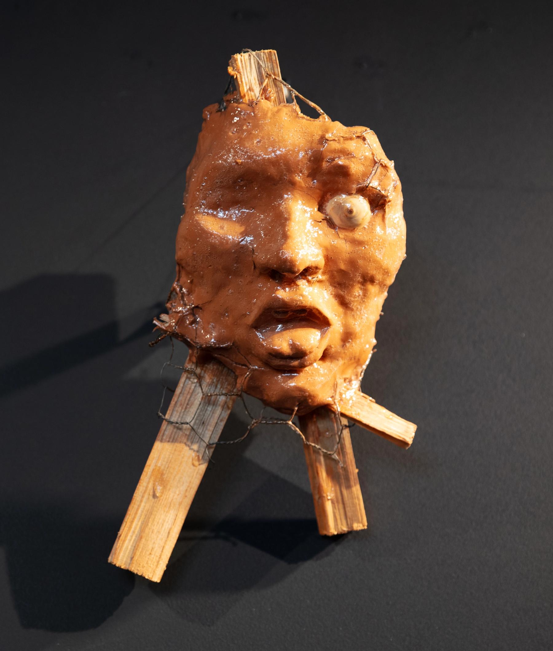 grotesque orange waxy gargoyle mask with one eye and tongue sticking out