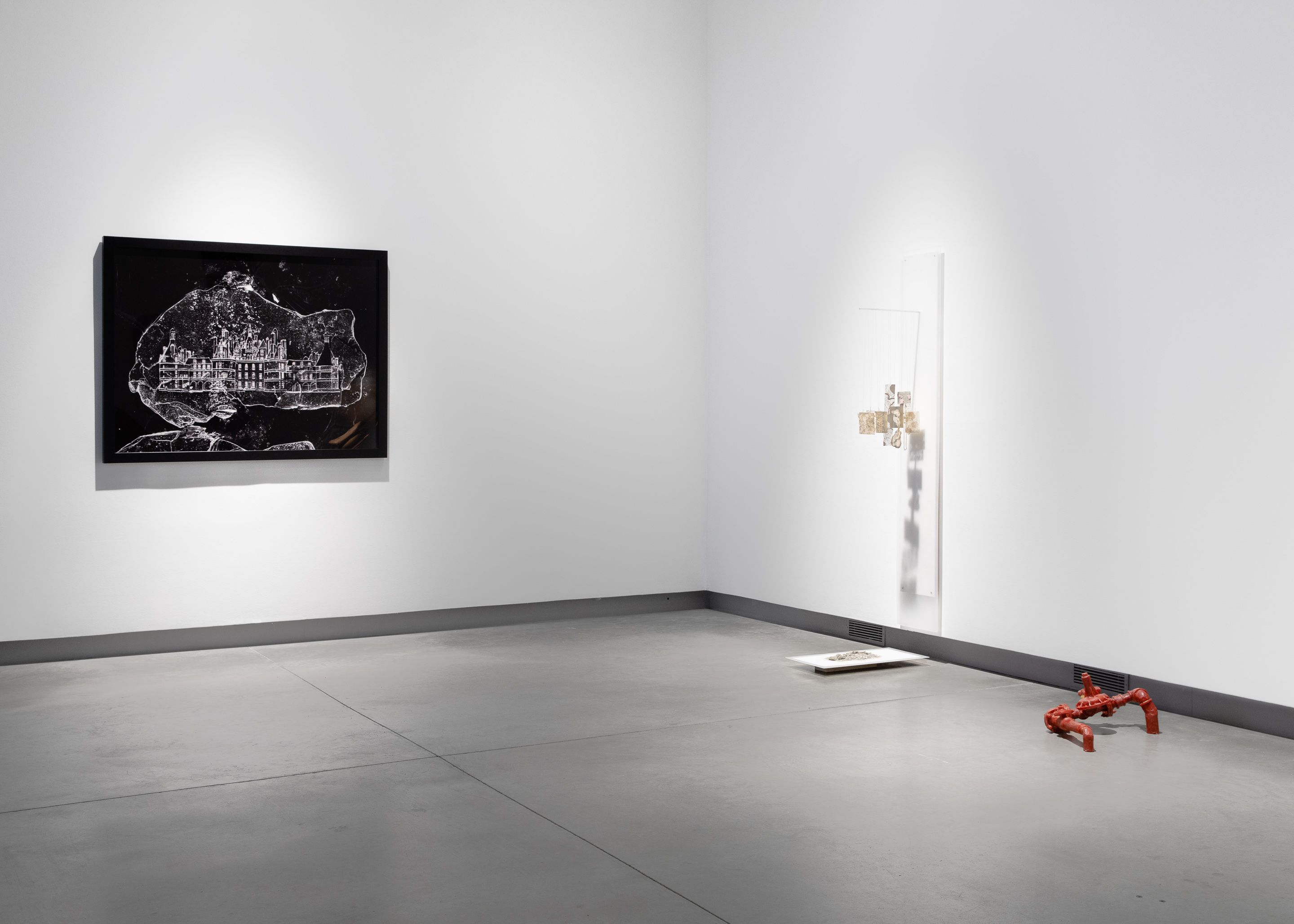 Installation view of a black and white print next to a hanging metal sculpture.