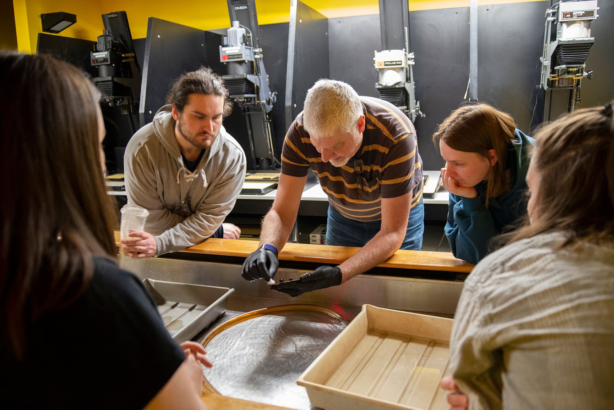 A professor giving a demo to students on Tintypes in the photography darkroom.