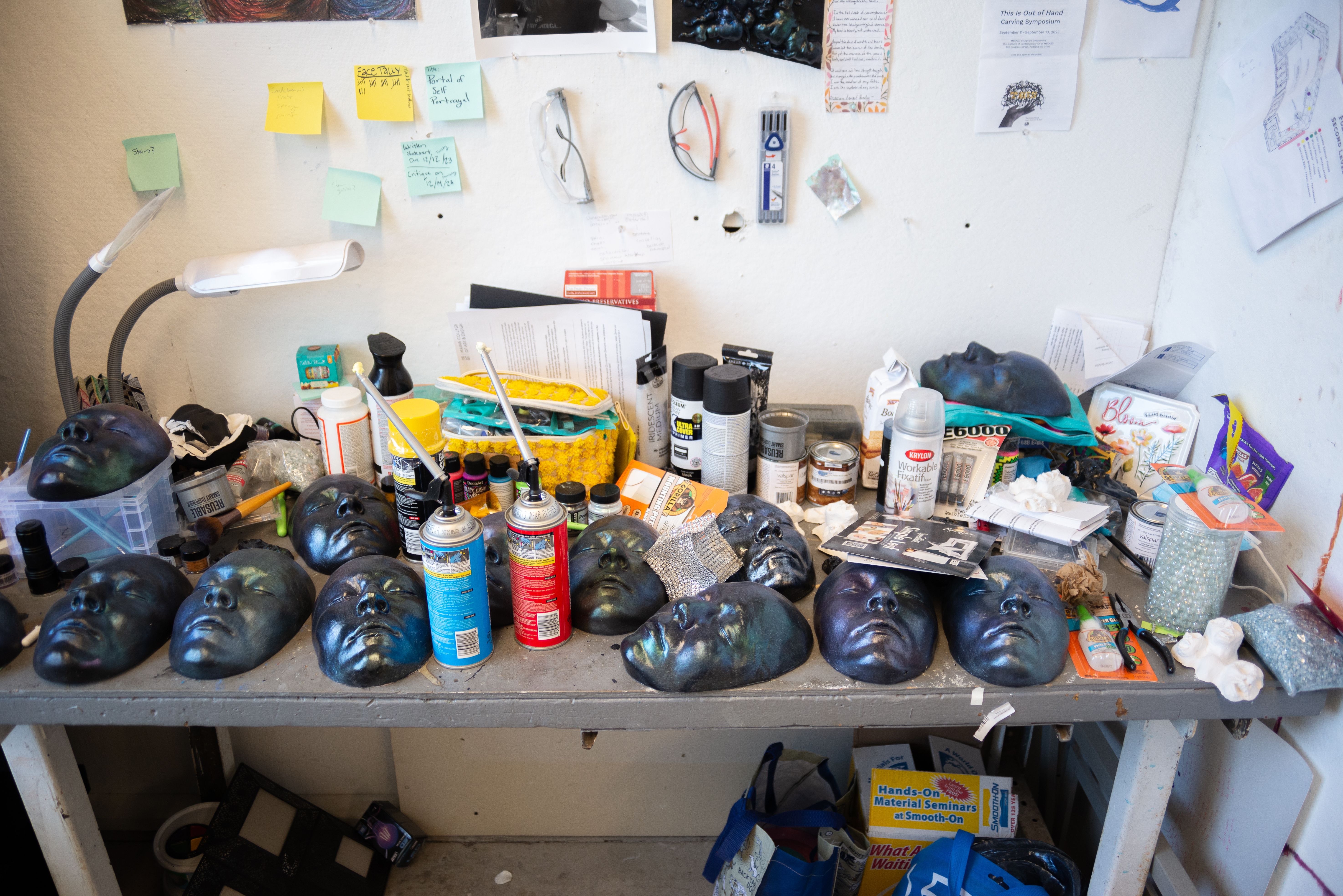 A workspace table covered with spray-paint cans and black masks.