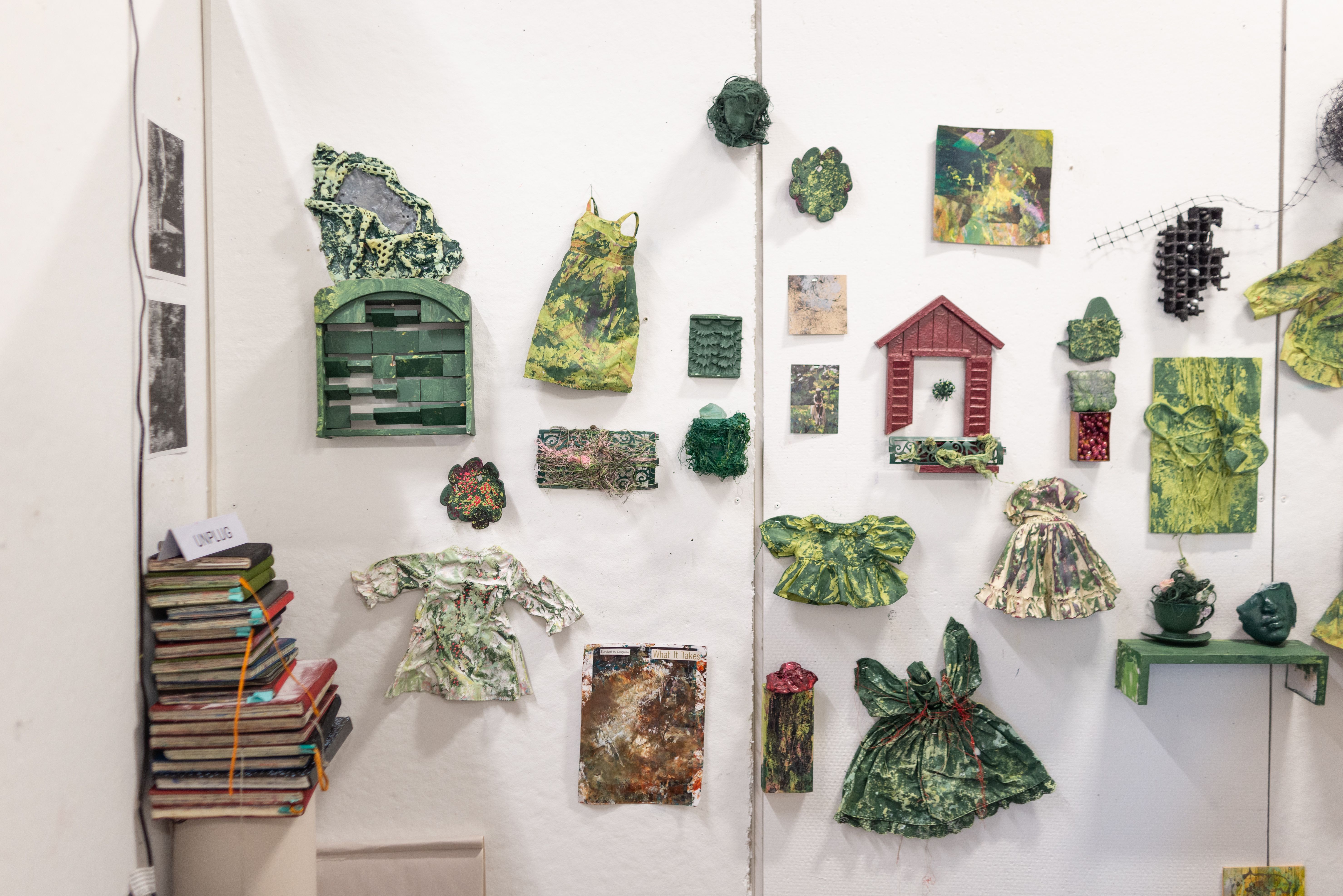 MFA Studio space with green painted paper and fabric pieces resembling homes and dresses.