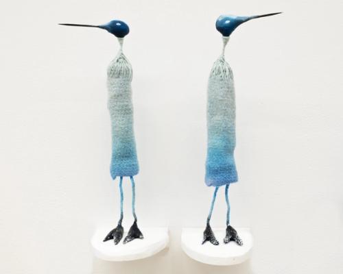 An installation of two long bird sculptures, facing away from each other.