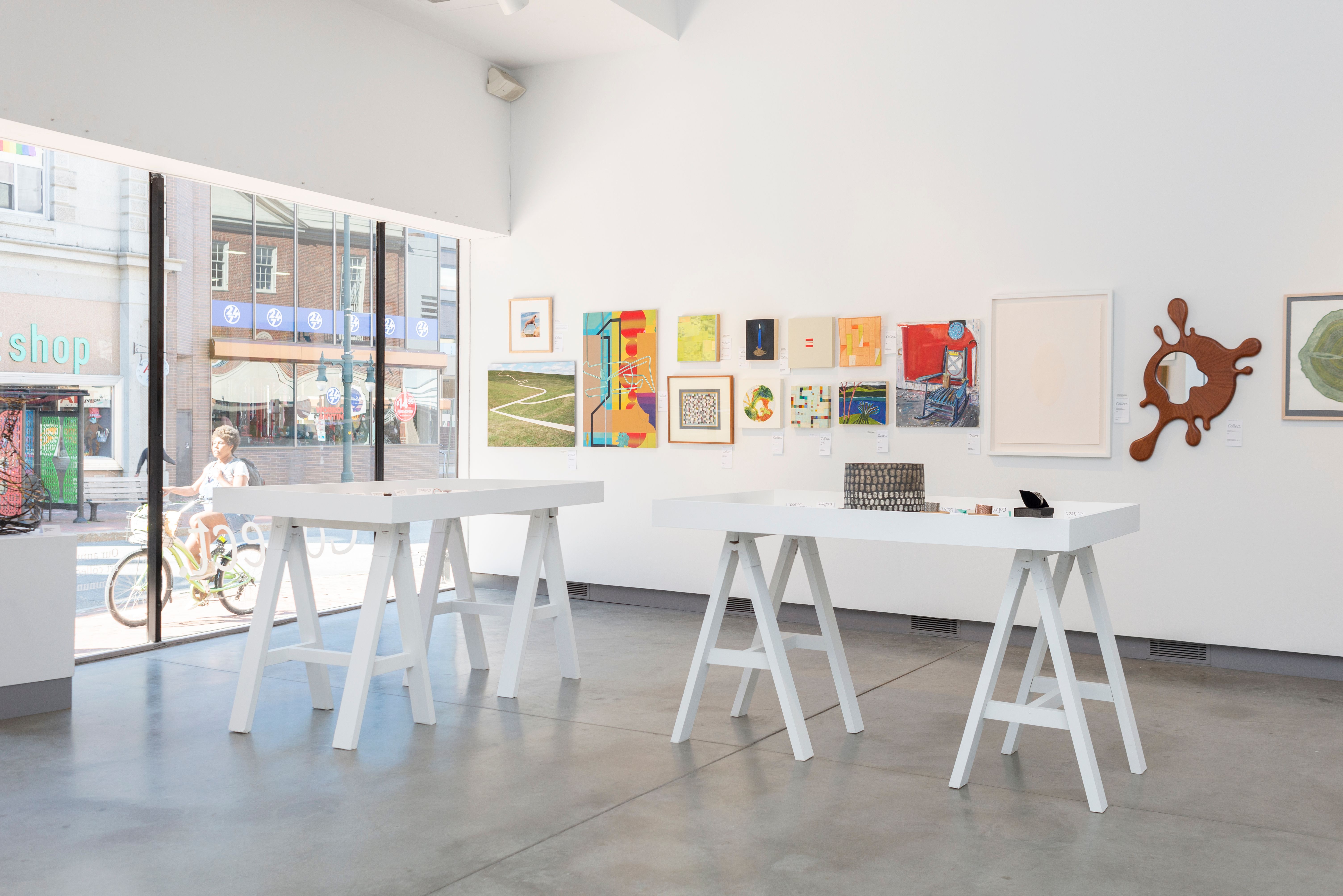 View of the ICA with many pieces of art displayed on the walls and two tables.