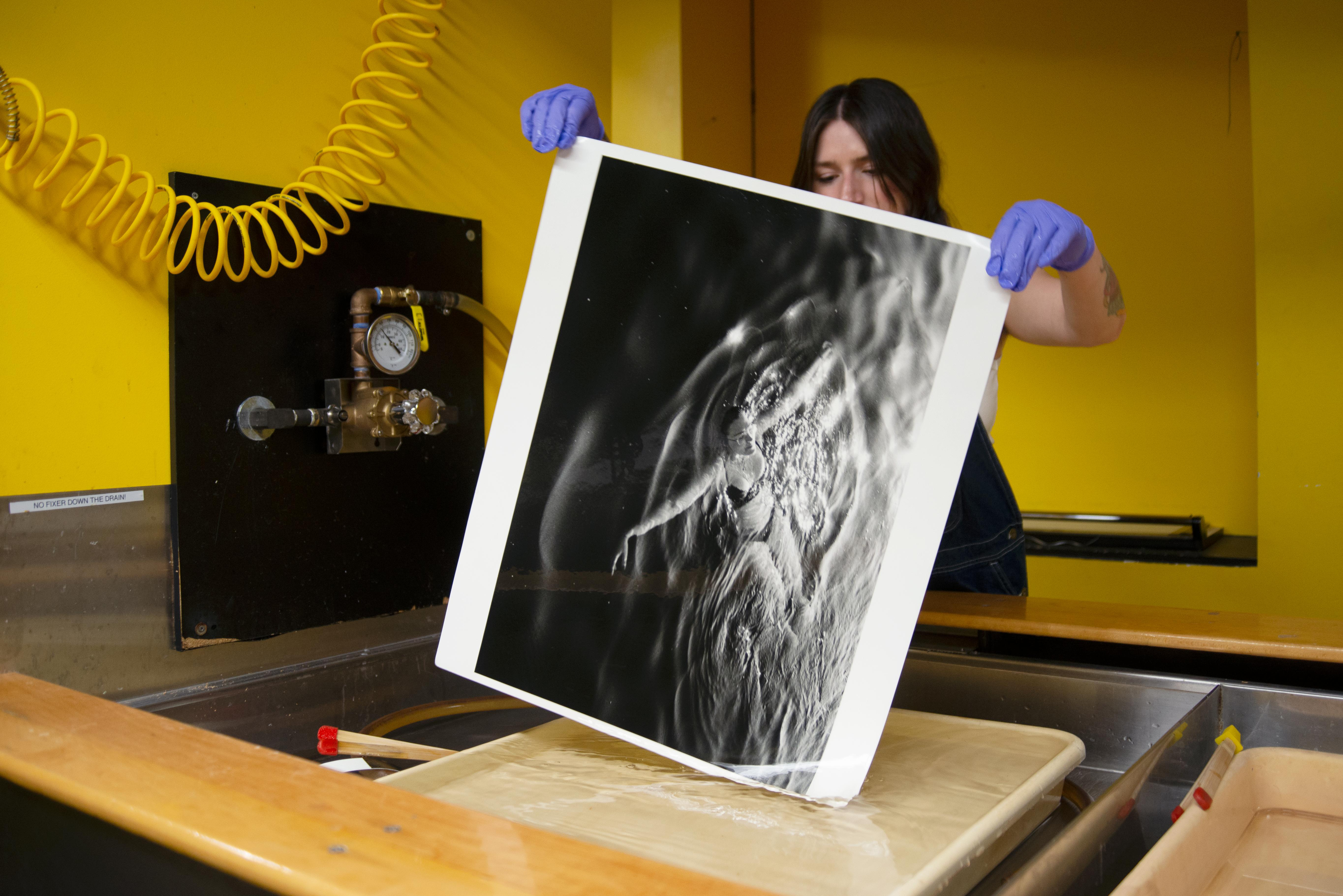 A student working on developing a large black and white photograph of a feminine figure floating in the ocean.