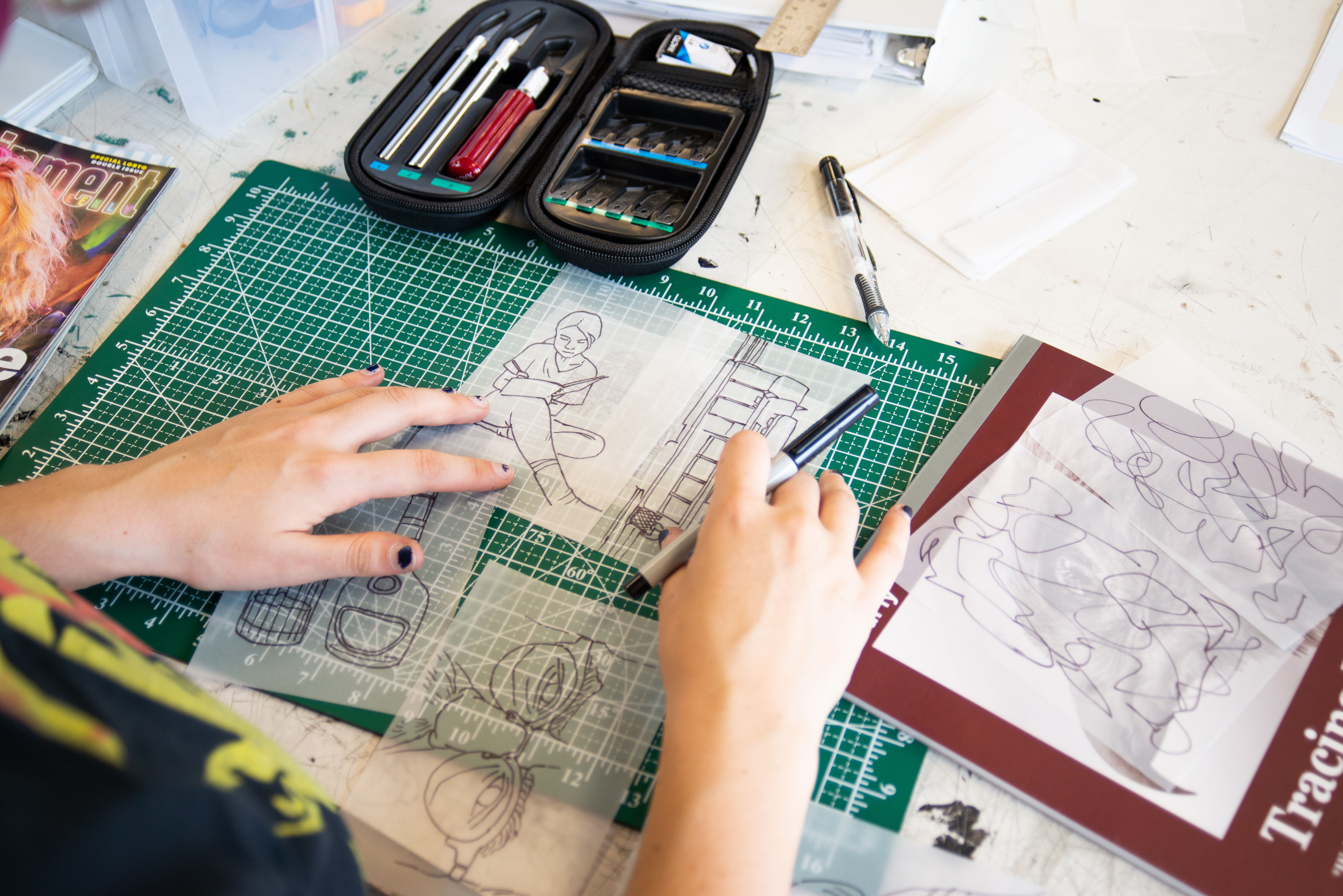 Student aligning drawings on tracing paper on top of a cutting map with a pen in their hand