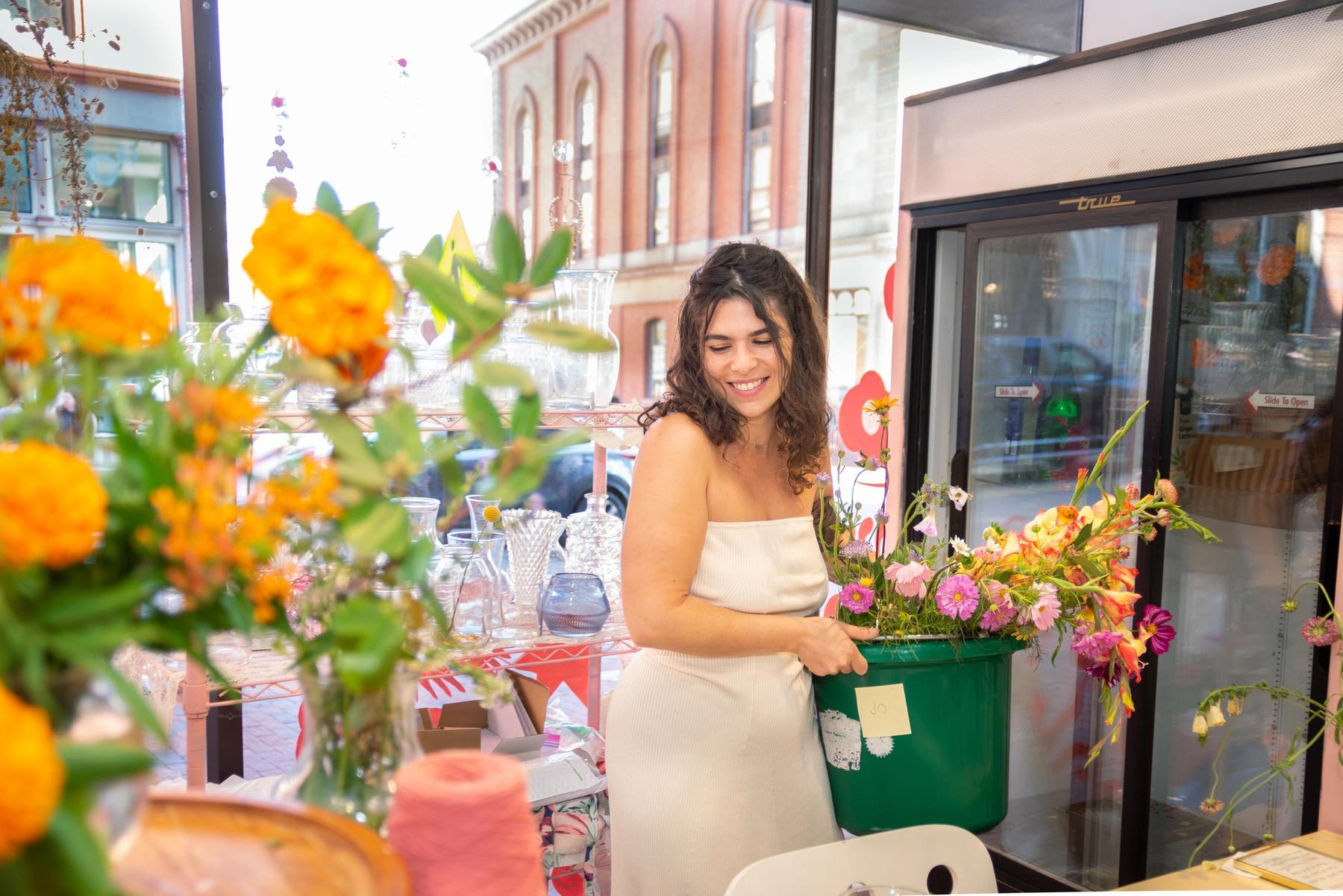 Jodi Ferry smiling, surrounded by flowers in her pop-up shop.