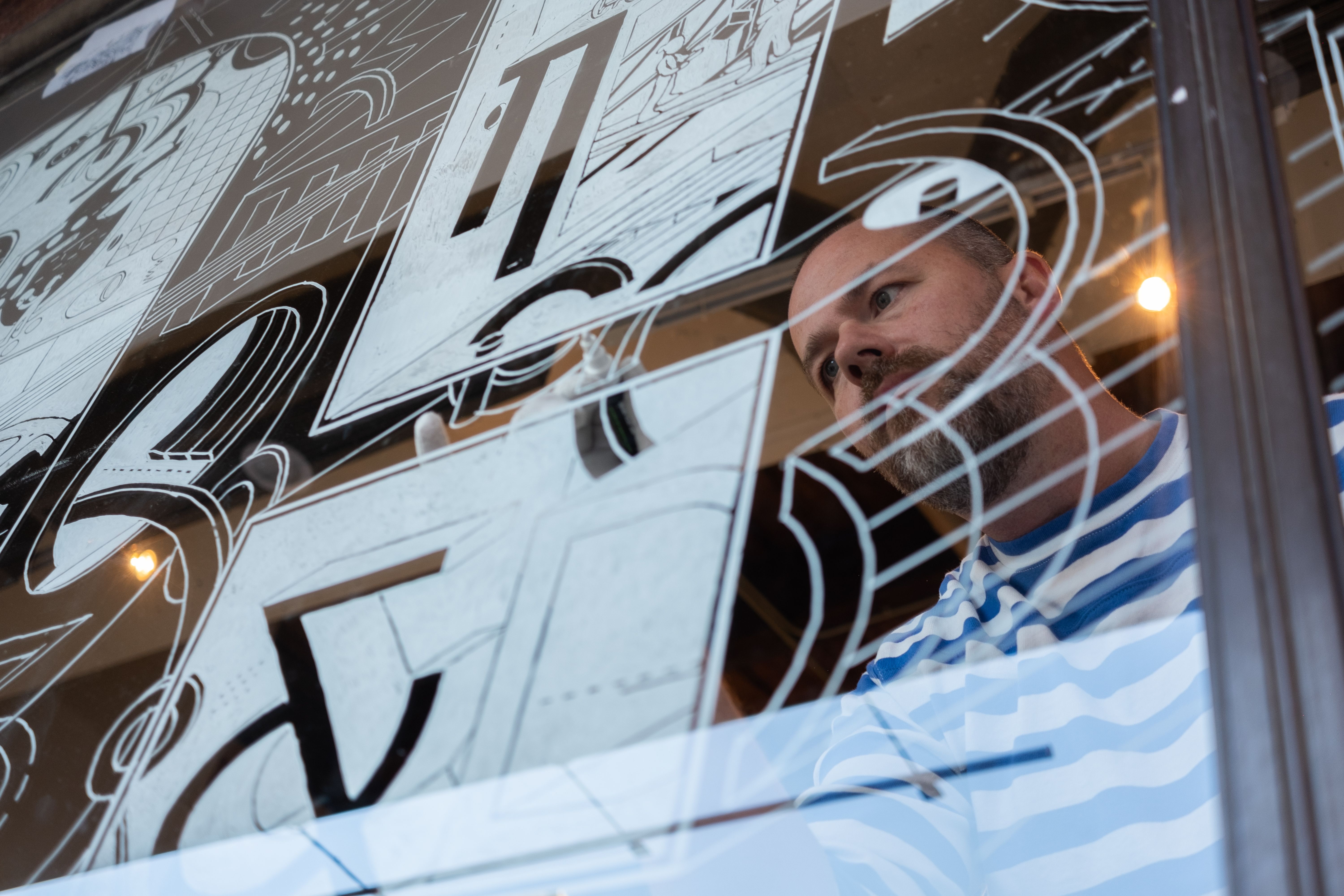 Faculty member working on an illustration on a window.