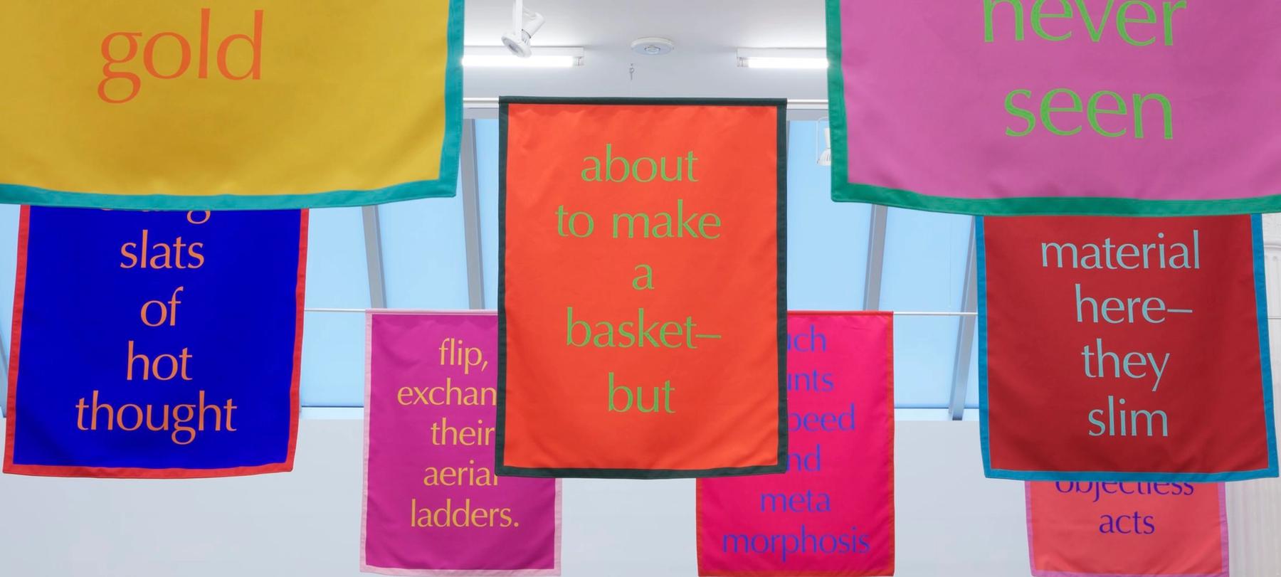 Colorful typographic banners hanging from the ceiling by Renée Green.