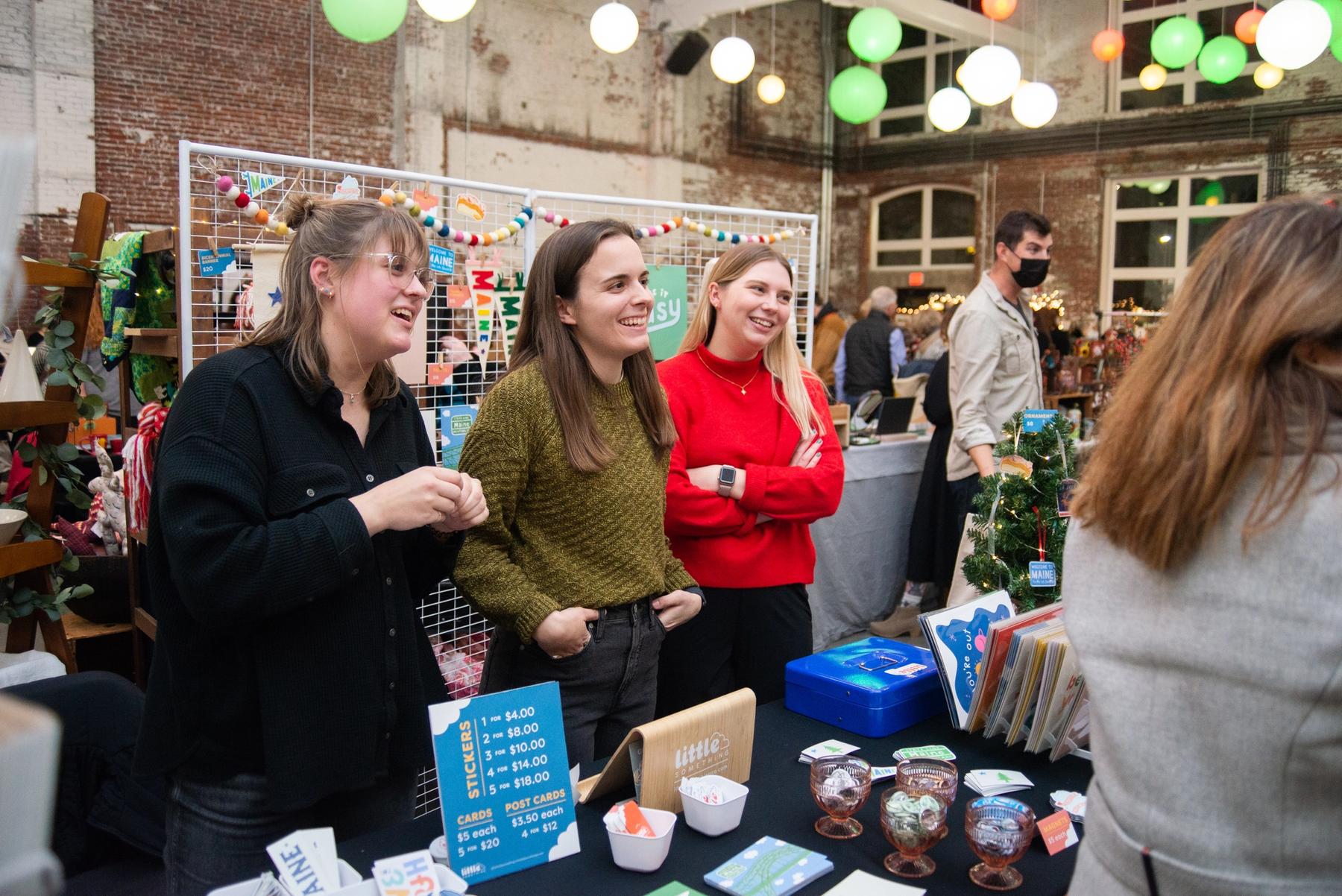 Three artists selling their work during a holiday sale.