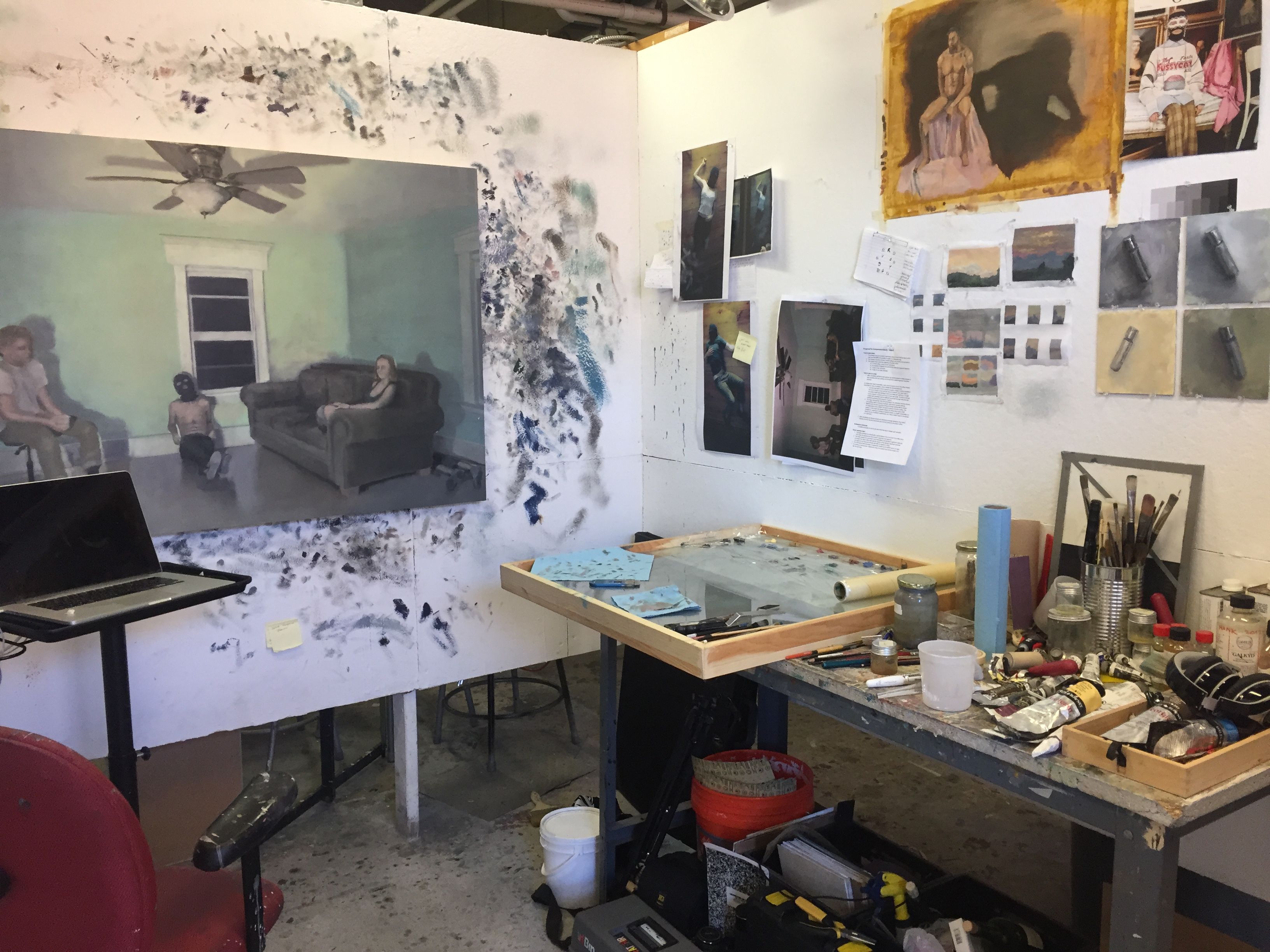 View of a painting studio space with a large painting of a living room, smaller figure studies, and a large collection of brushes.