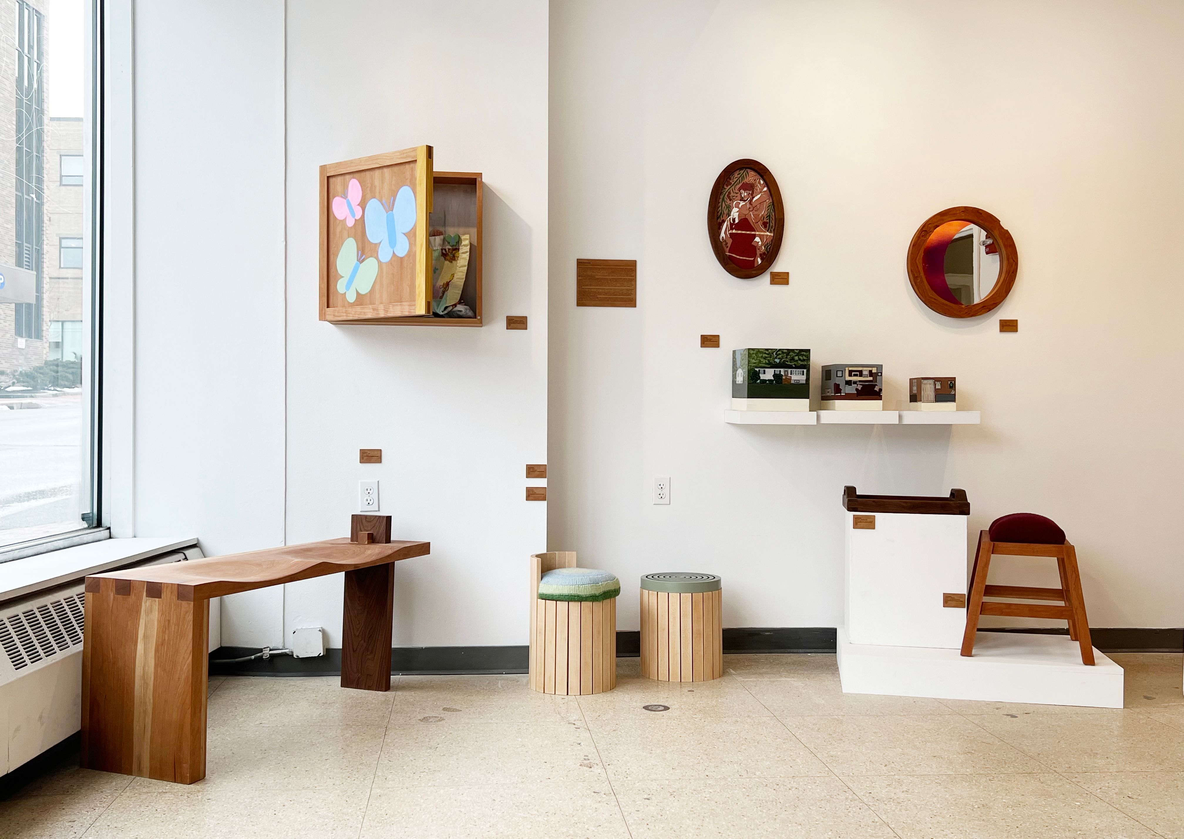 An installation of wooden furniture, including a bench, stools, mirrors, and a cabinet.