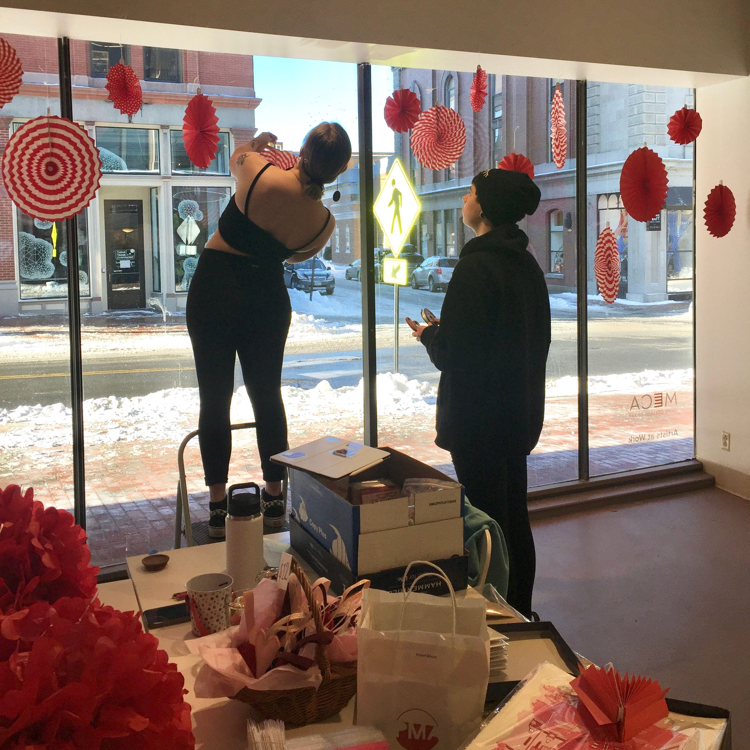 Students installing red decorations in the Porteous Building entryway windows.