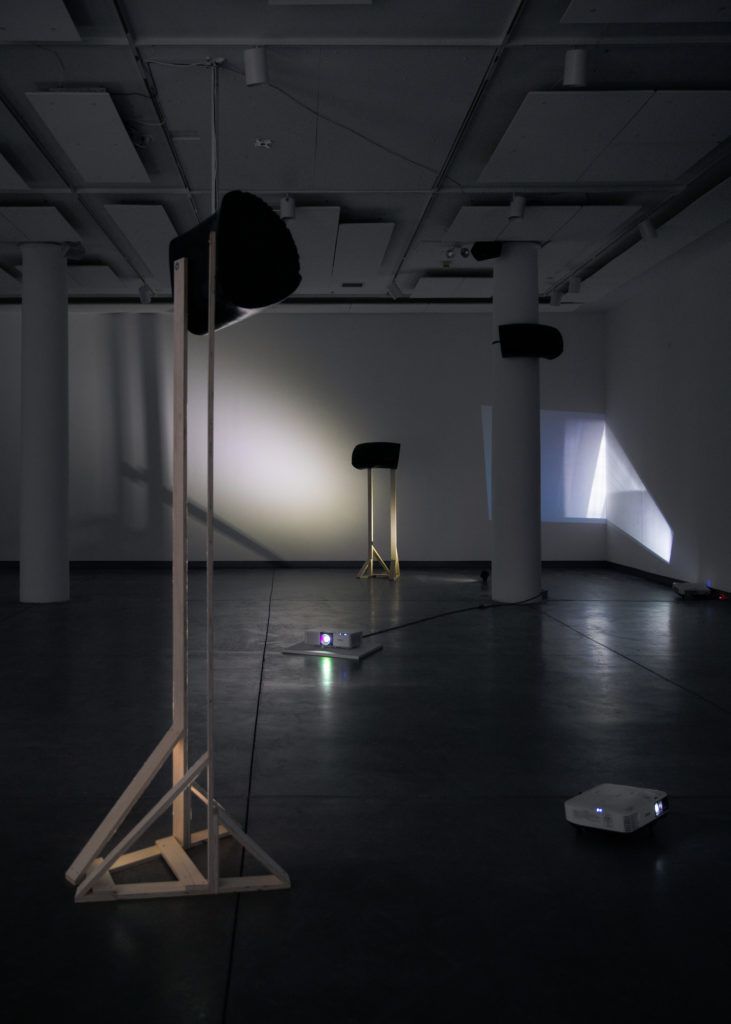 Gallery view of two sculptures, a distorted projection, and two projectors on the floor.