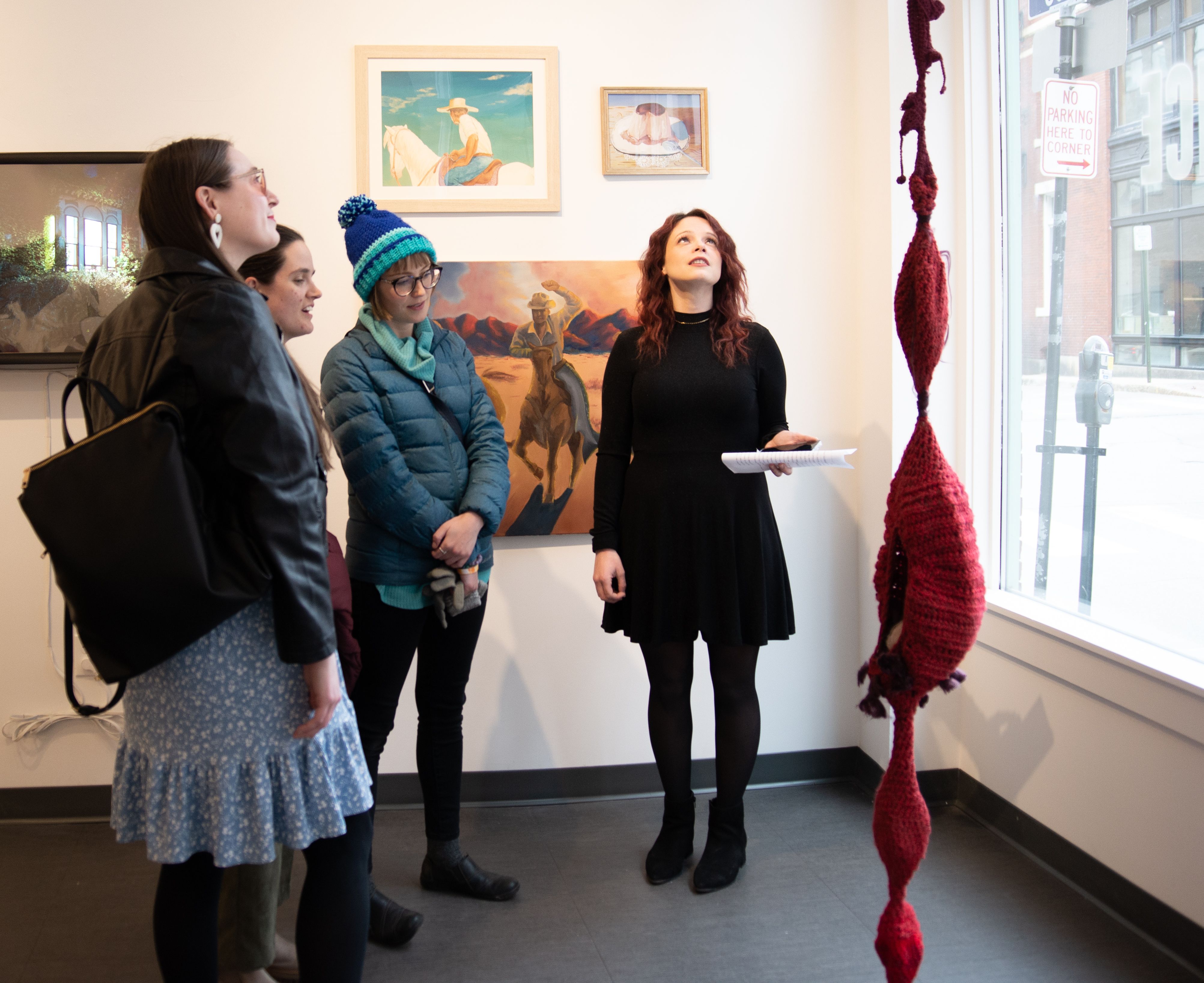 Four people looking at a red hanging fiber sculpture in the 49 Oak gallery.