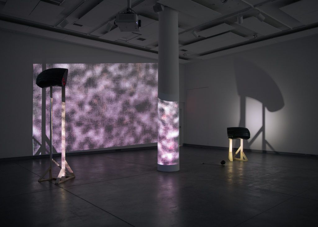 Gallery view of a large purple distorted projection next over two sculptures.