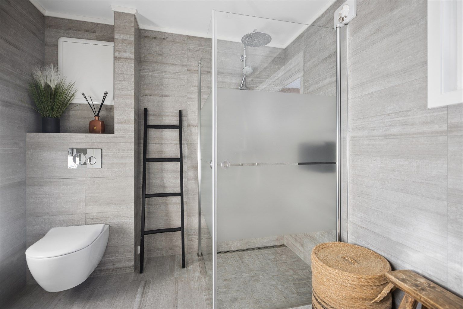 Flislagte overflater, behagelig gulvvarme og stilren servantinnredning med speil og sidelys. Badet har også vegghengt toalett og et elegant dusjhjørne med både hånddusj og regndusj.
