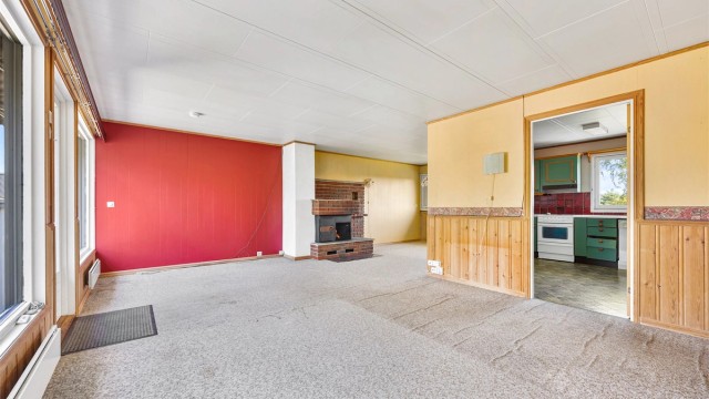 Romslig stue med plass til flere sittegrupper og adkomst til kjøkkenet.