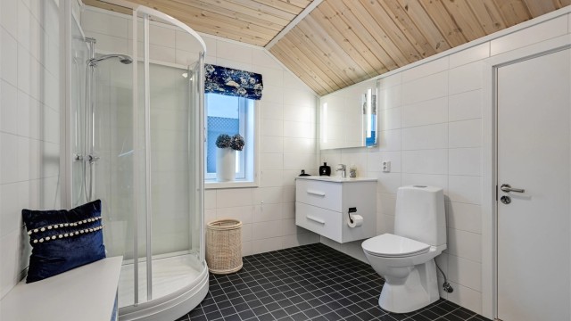 Et flislagt bad med varmekabler i gulv, innredet med heldekkende servant, gulvmontert toalett og dusjkabinett.