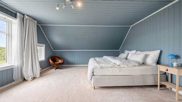 Stort soverom i loftsetasjen med vegg-til-vegg-teppe og malte panelvegger.