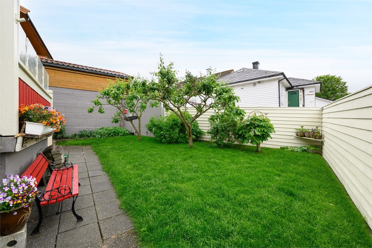 Tomt opparbeidet med belegningsstein, steinheller, diverse beplantninger, plenareal.