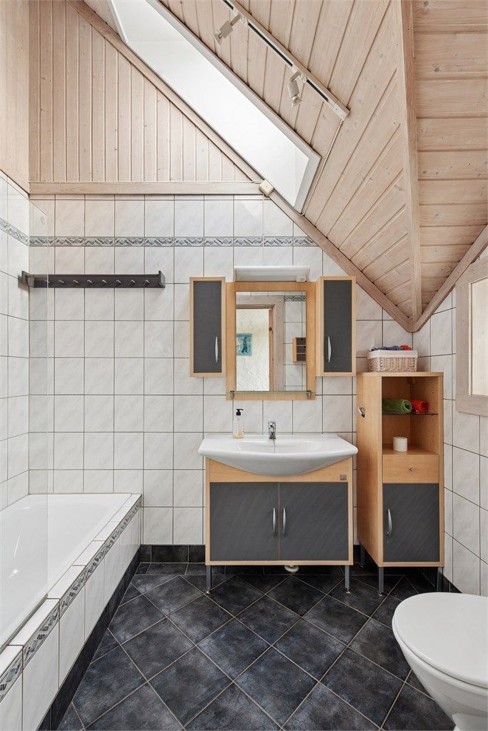 Hovedbadet er flislagt med gulvvarme og bestående av badekar, servant og toalett. Også her finner vi de arkitektoniske linjene i taket.