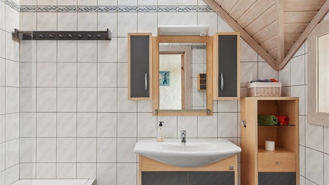 Hovedbadet er flislagt med gulvvarme og bestående av badekar, servant og toalett. Også her finner vi de arkitektoniske linjene i taket.