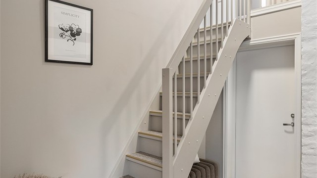 Den interne trappen leder opp til loftsplanet, hvor skrå himlinger, synlige konstruksjonselementer og takvinduer skaper en lun og skjermet atmosfære.