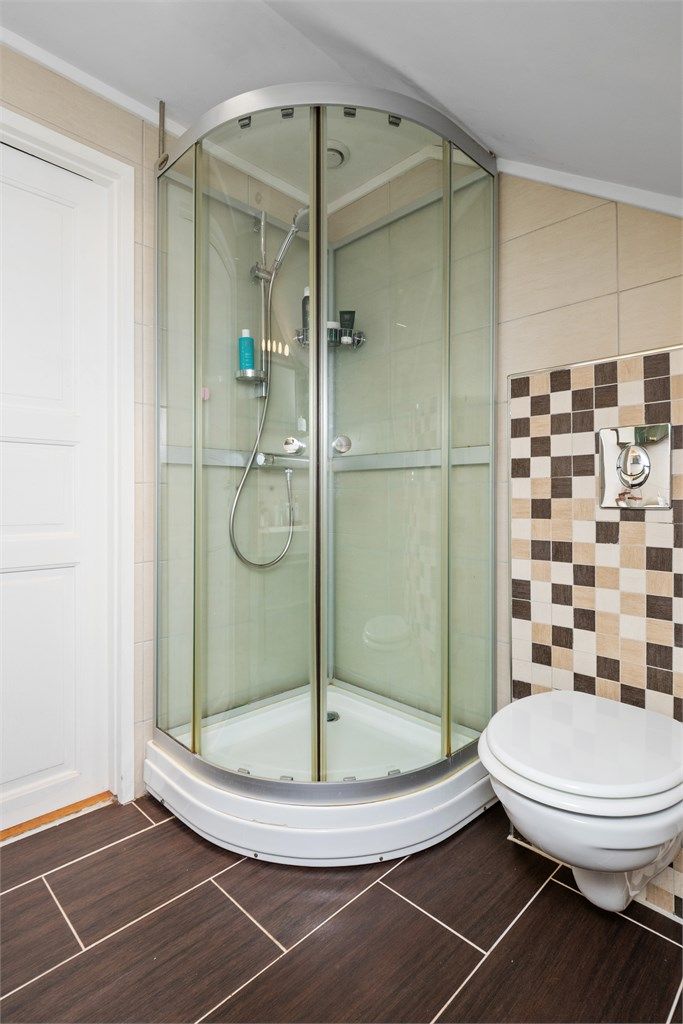 Innredningen består av en heldekkende servant på brun skuffeseksjon, matchende speilhylle, et veggmontert toalett og praktisk dusjkabinett.