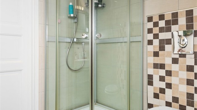 Innredningen består av en heldekkende servant på brun skuffeseksjon, matchende speilhylle, et veggmontert toalett og praktisk dusjkabinett.