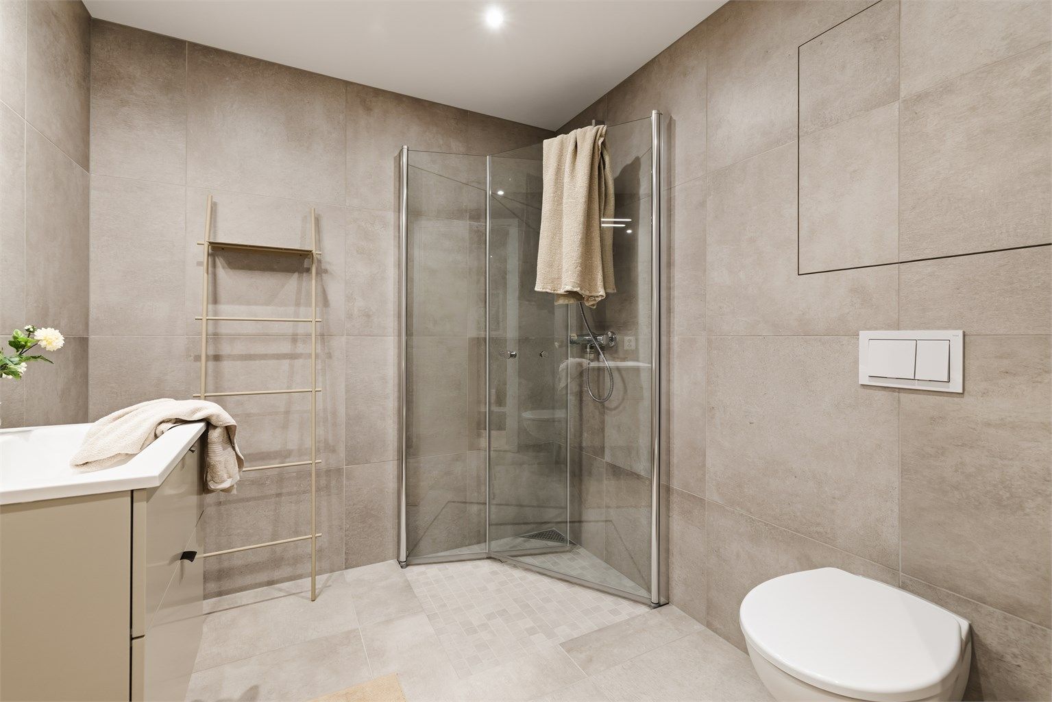 Videre har badet dusjhørne med innfellbare glassdører og vegghengt toalett.