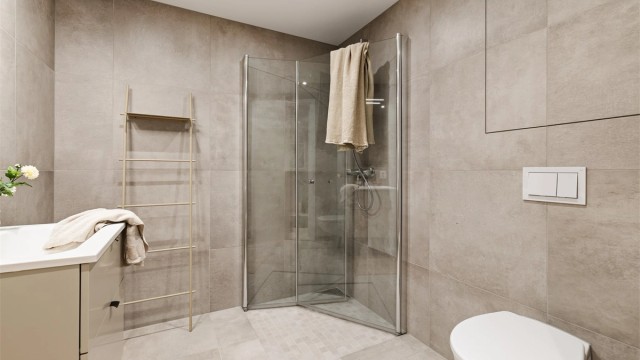 Videre har badet dusjhørne med innfellbare glassdører og vegghengt toalett.