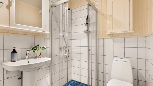 Bad tilknyttet utleiedelen mot øst. Badet har flislagt gulv med gulvvarme, en kombinasjon av panel og flis på veggene samt et praktisk dusjhjørne.