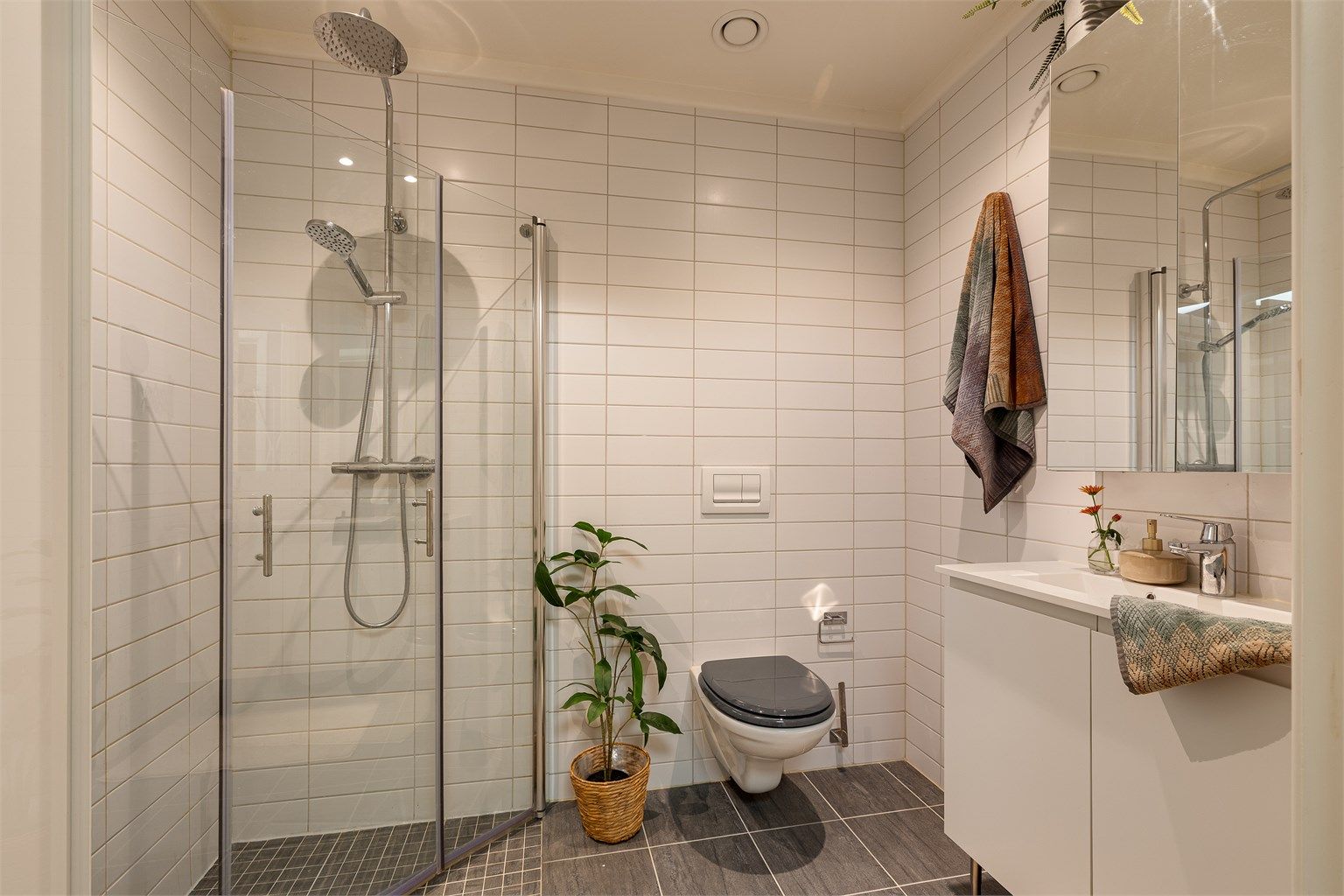 Badet i hovedetasjen har også vegghengt toalett, innfellbare glassdører i dusjen, og servant med speilskap over samt skap under. Downlights i himling.