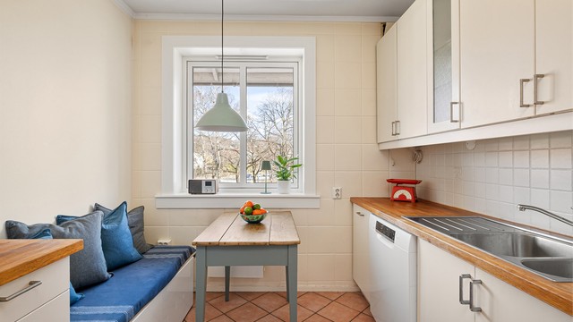 Separat kjøkken med plass til spisebord og sittebenk ved vinduet. Fra vinduet er det koselig utsyn over nabolaget og opp mot Grefsenåsen