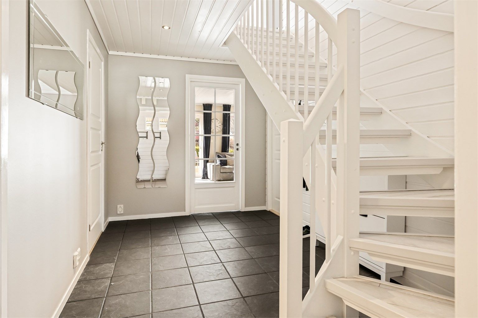 Gangen ønsker velkommen med flislagt gulv og trapp opp til andre etasje. Døren i glass slipper lyset gjennom fra stuen.