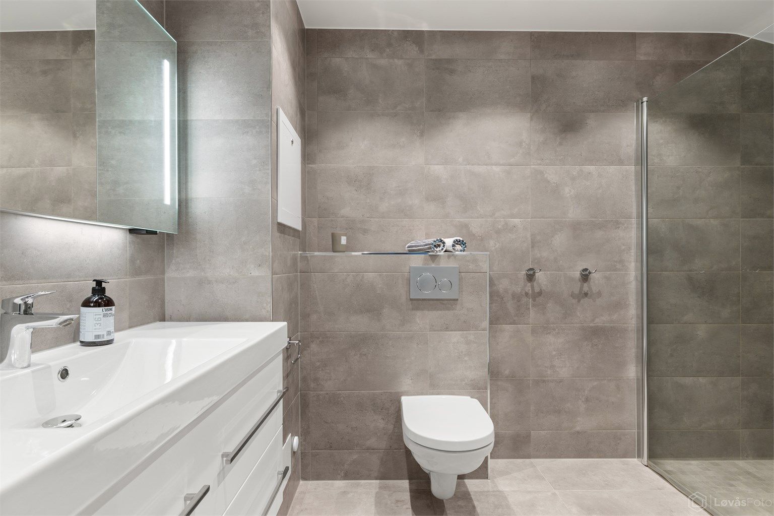 Romslig og innbydende familiebad fra 2018 med moderne standard og praktiske løsninger. Badet har flislagt gulv med gulvvarme, flislagte vegger og nedsenket himling med downlights som gir behagelig belysning.